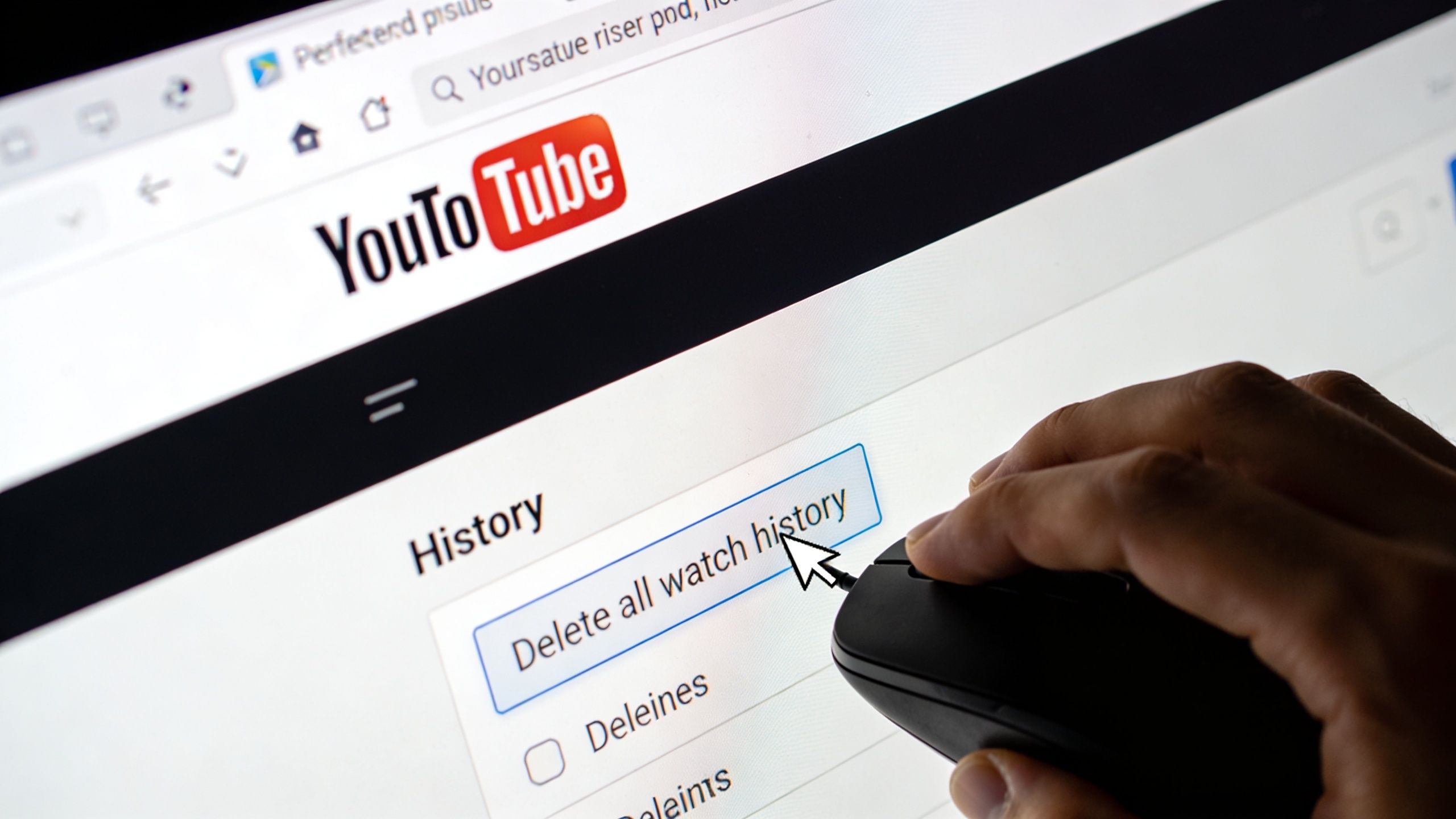A hand using a computer mouse to click on the Delete all watch history button on YouTube.